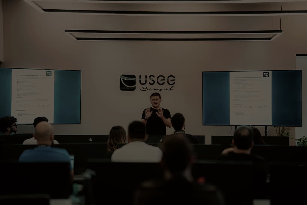 Encontro na Usee Brasil: um apresentador fala para empresários sentados às mesas, com telas de apresentação ao fundo